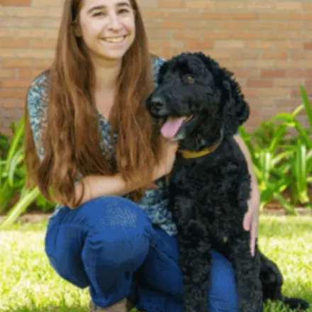 Lauren Hirsch kneeling next to a black dog